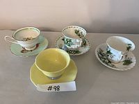 Four assorted Royal Albert teacups with matching saucers displayed on a flat surface, showing different floral and colored designs.