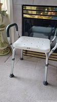 Front view of the shower chair showing white seat with textured surface and padded armrests.