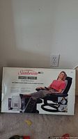Front view of Sunbeam Dossier Masseur massage pad box showing woman using the product on a chair reclining with footrest.