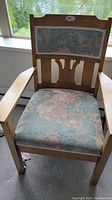 Front view close-up of vintage wooden arm chair with floral fabric on backrest and seat.