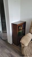 Full view of wooden bookshelf positioned against wall next to beige recliner, with books on shelves