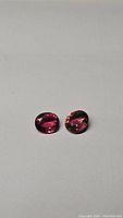 Photo of two oval cut purple pink tourmaline gemstones placed on a plain background, showing their color and clarity.