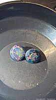 Pair of small round black opal cabochons in a dark tray showing vibrant rainbow flashes under light.