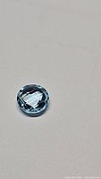 Close-up photo of 2.19ct round checkerboard cut Swiss blue topaz gemstone on neutral background showcasing its color and cut.