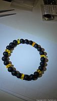 Photo showing the bracelet laid flat on a surface with alternating black lava stone beads and golden yellow Baltic amber beads.