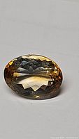 Close-up of large faceted golden citrine gemstone showing oval cut and facets reflecting light.