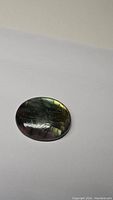 Oval cabochon natural labradorite gemstone on white background showing dark surface with subtle iridescent flash.