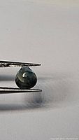 Pear cut blue green sapphire held with tweezers showing size and color.