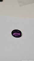Oval cut deep purple amethyst gemstone photographed on white background showing color and clarity.