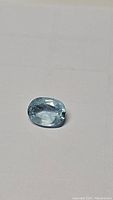 Close-up photo of the natural oval cut aquamarine gemstone showing its sky blue color and faceting.