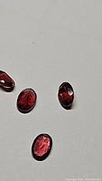 Four oval cut cherry red garnet gemstones laid on a white background, showing the rich deep red color and faceted cuts.