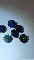 Photo showing six small round cut natural Ethiopian black opal gemstones with dark bases and vibrant multi-colored flashes under lighting.