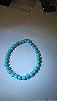 Photo of the turquoise gemstone bracelet showing its round blue beads and stretchy design against a plain background.