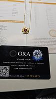Photo of garnet colored moissanite necklace pendant lying on a GRA certificate card and grading report.