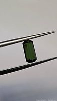 Photo of a natural untreated green tourmaline octagon cut gemstone held by tweezers