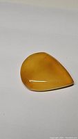 Close-up image showing smooth polished golden yellow onyx gemstone with teardrop shape and bright reflective surface.