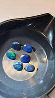 Photo of six natural black opal gemstones with deep dark base color, polished oval and rounded shapes showing bright rainbow flashes.