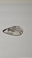 Pear-shaped black rutilated quartz gemstone with visible needle-like black rutile inclusions on white background.
