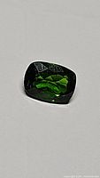 Rectangular cushion-cut deep green chrome diopside gemstone with good clarity and light reflection.