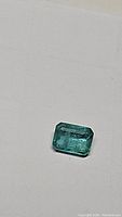 Emerald cut emerald gemstone placed on white surface for clear view of cut and color