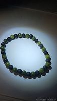 Full view of the round bead bracelet showing alternating green jade and black lavastone beads arranged on an elastic band.