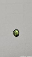 Oval shaped green sapphire gemstone placed on a flat surface for clear top view