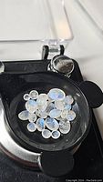 Top view of polished mixed size natural Rainbow moonstones in black tray highlighting the blue flash effect.