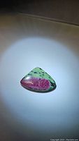 Natural ruby zoisite gemstone showing pink ruby embedded in green zoisite matrix with black spots.