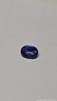 Oval cut deep blue to purple natural tanzanite gemstone lying on a light background, clear view of color and slight inclusions.