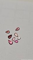 Top down photo of nine pear shaped pink tourmaline gemstones on white background showing various shades and cuts.