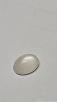 Close-up photo of single oval cabochon white moonstone gemstone on plain background, showing translucency and surface polish
