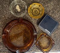 Top-down view of four ashtrays and a BCGRAIL lighter case arranged on a granite countertop.