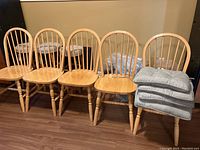 Five wooden kitchen chairs arranged in a row with five striped cushions stacked on one chair.