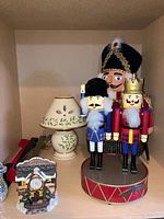 Wooden nutcracker figurines, ceramic candle holder with shade, and ceramic clock figurine displayed together on shelf