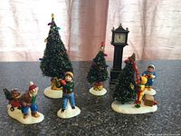 Photo showing all Christmas miniature decorations including four child figurines, three bottle brush trees, and clock tower.