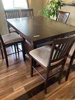 Wide angle photo showing 6 matching bar height chairs around a dark wood square dining table on wood floor.