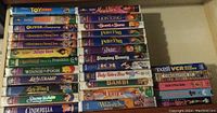 Photo showing stack of Disney VHS tapes including Toy Story, Aladdin, Dumbo, Lion King, Oliver Company, Sword and Stone, Peter Pan, Babe, Sleeping Beauty and others.