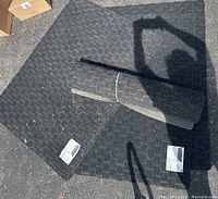 Four black utility mats displayed on a garage floor; two mats laying flat and one rolled and tied; mats have diamond textured pattern surface.