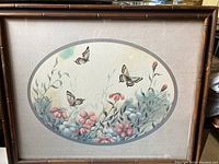 Framed print with wooden bamboo style frame showing butterflies over pink flowers and green leaves inside an oval mat.