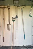 Gardening tools hanging on wall including metal rakes, pitchfork, airrater, and weed picker