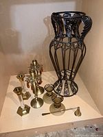Photo of assorted metal and glass candle holders, metal candle snuffer, and large black metal scroll umbrella stand on light wood surface.