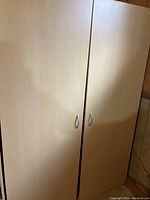 Front view of the closed large wooden storage cabinet showing two doors with silver handles.