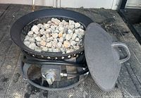 Photo of the propane fire pit bowl filled with lava rocks, control knob, and coiled hose at bottom.