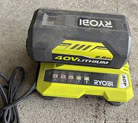 Ryobi 40V 2.6Ah Lithium battery on top of Ryobi 40V battery charger showing dust and wear from storage.