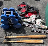 Set of sports items including blue hand weights stacked, Adidas gym bag, Blade Runner rollerblades, and two wooden baseball bats.