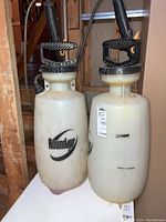 Photo showing two handheld Roundup sprayers with black handles and braided spray hoses on white plastic containers.