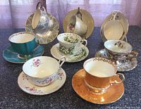 Eight varied teacups and saucers displayed on a surface with stands, showing different ornate floral and gold detailing
