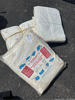 Three white reinforced tarpaulins; two in original packaging showing Interline branding and product details; third tarp folded without packaging