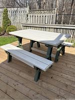 Two plastic resin benches joined to form a picnic table on a wooden deck outdoors surrounded by a fence and trees.