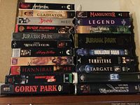 Stack of VHS movie tapes showing titles such as Apocalypse Now, Gladiator, Hancock, Blade Runner, Jurassic Park, and more.
